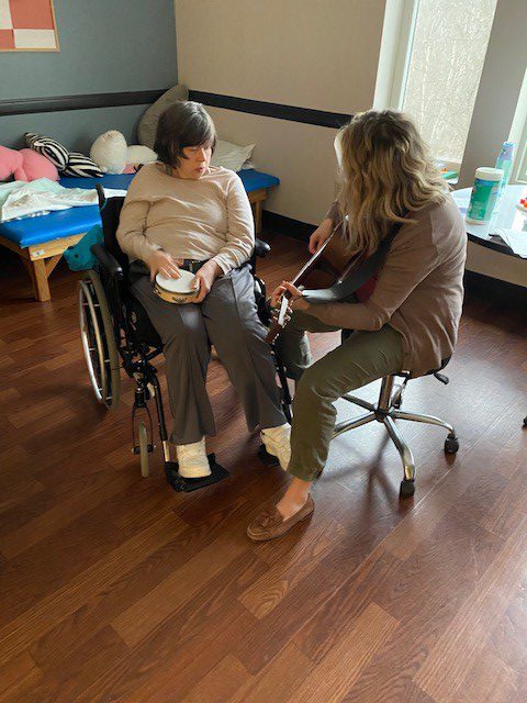 One woman playing the guitar while another with disabilities listens