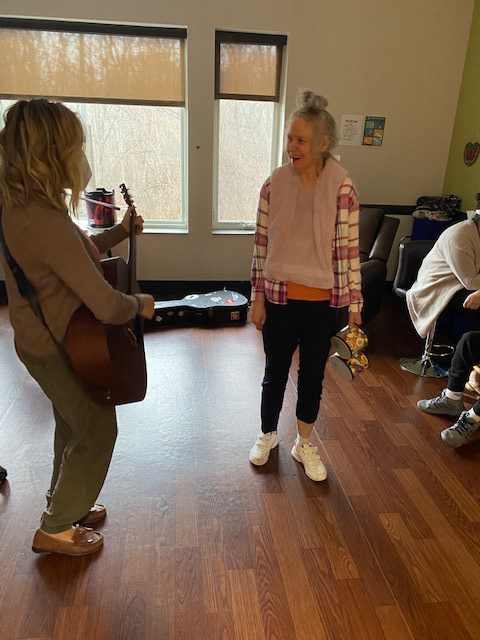 One woman playing the guitar while another with disabilities listens